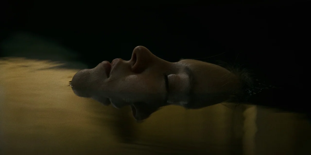 Immaculate (2024) movie still: closeup — A person floats in dark, still water at night. Only the profile of their face is visible above the surface,…