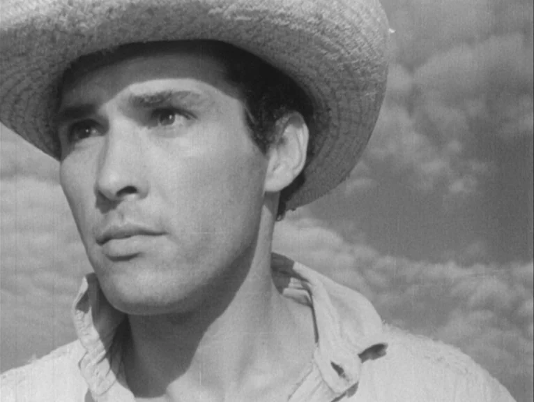 Redes (1936) movie still: closeup — An outdoor environment under a clouded sky with visible film grain. A man wearing a straw hat gazes toward the…
