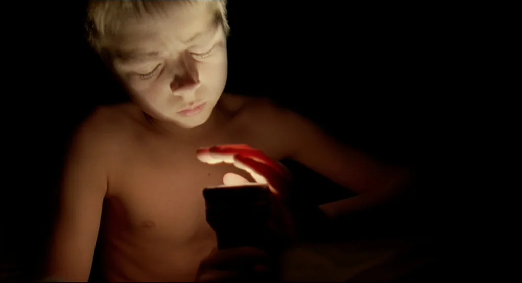 The Tree Of Life (2011) movie still: closeup — A dark space lit only by the concentrated beam of a handheld flashlight. A shirtless young boy sits…