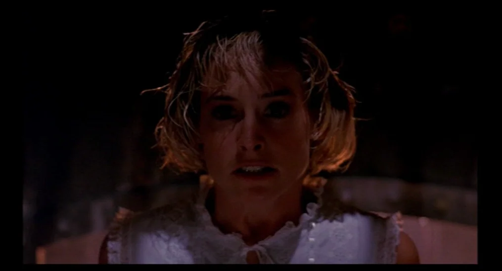 A Nightmare On Elm Street (1984) movie still: closeup — A dimly lit room with the subject centered against a black background. The woman faces the…