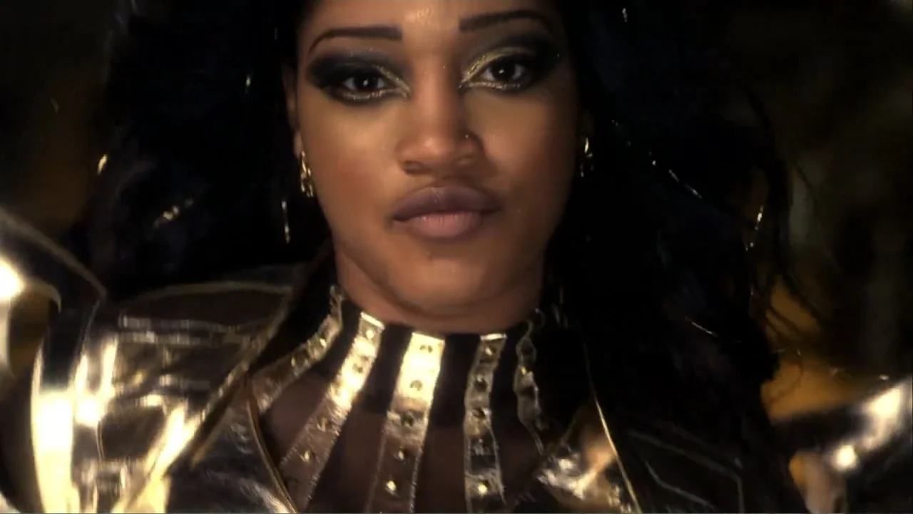 Rags (2012) movie still: closeup — A close portrait of a woman in metallic gold armor against a dark background. She faces forward while the camera…