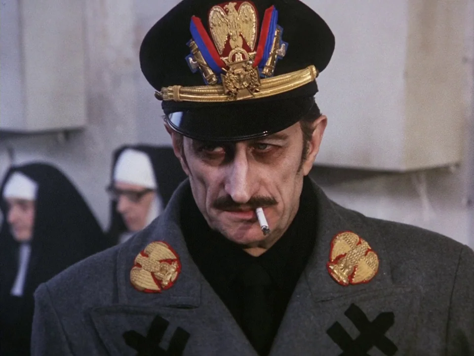 The Clowns (1970) movie still: medium — A man in military attire stands in a neutral-colored interior space with white walls. Two nuns wearing…