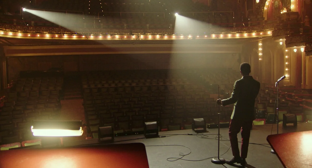 Detroit (2017) movie still: wide — An empty vintage theater interior with rows of plush seats and ornate gold detailing. A lone man in a dark blazer…