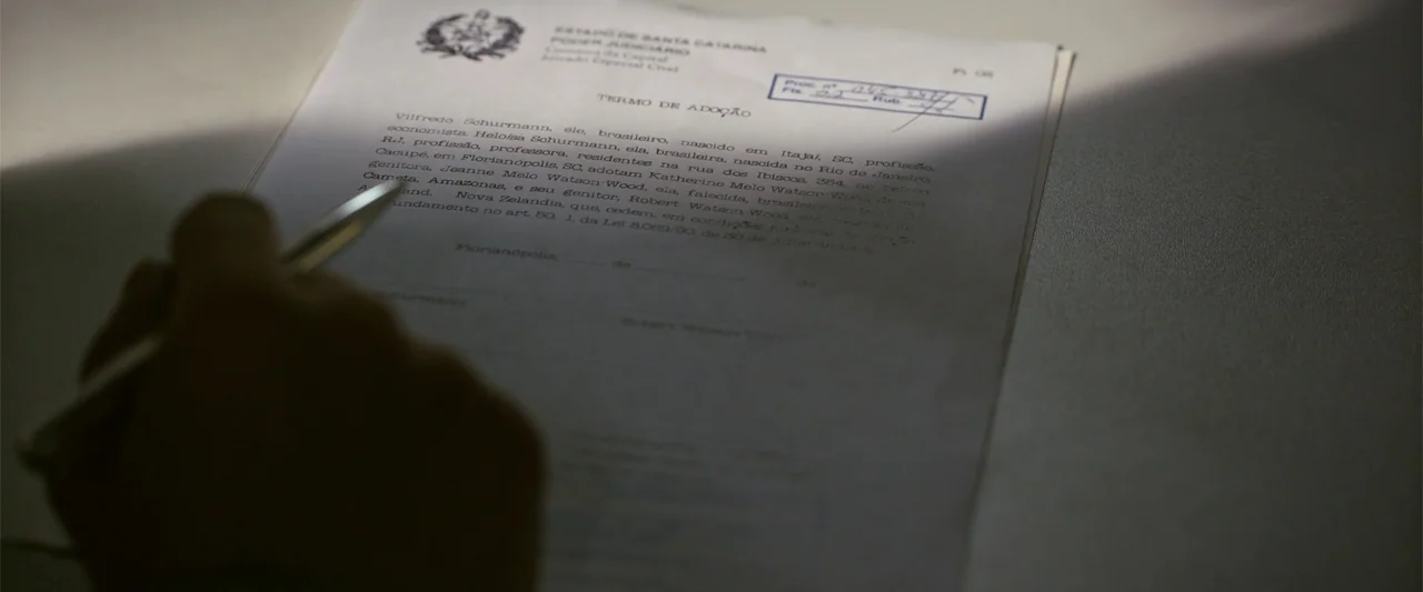 Dirty Little Secret (1998) movie still: closeup — A close-up view of a legal adoption document resting on a dark desk surface. A pen is held above…