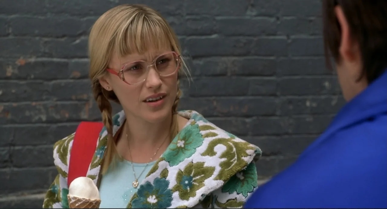 Little Nicky (2000) movie still: medium — A woman stands in front of a dark grey brick wall wearing a floral bathrobe. The woman holds an ice cream…