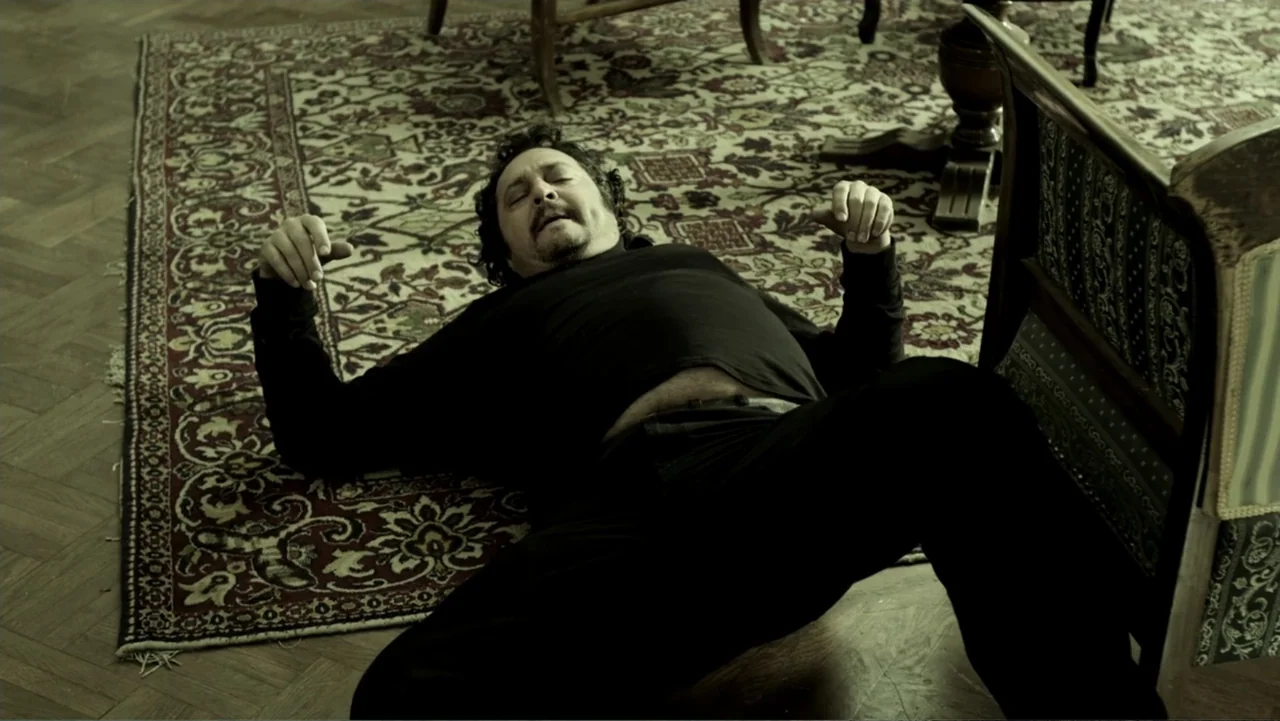 Assassination Games (2011) movie still: medium — A room with a polished wooden floor and a large, intricate, patterned rug. A man in black clothing…
