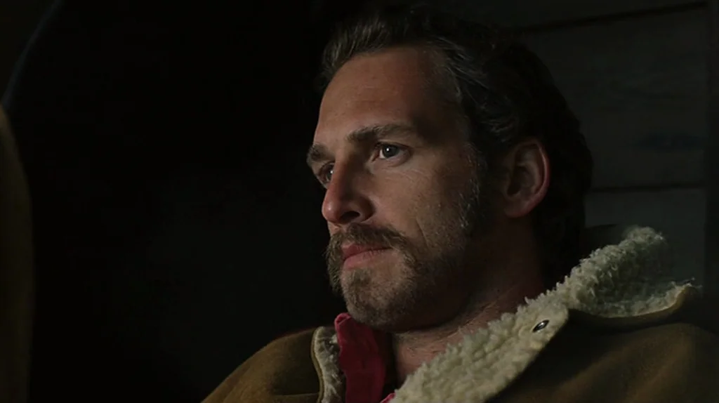 Undertow (2004) movie still: closeup — The interior of a vehicle at night with dark wood paneling visible. A man wearing a sheepskin coat sits in…