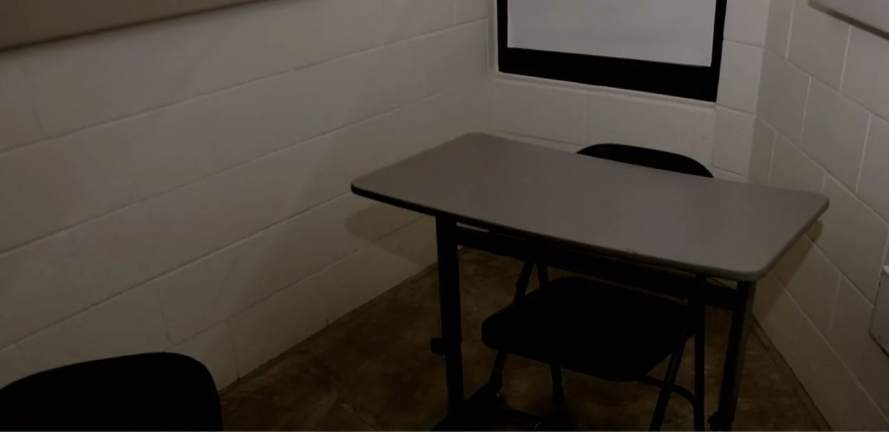 Doctors of the Dark Side (2011) movie still: wide — A spartan room features white concrete block walls and a gray folding table. Two folding chairs…
