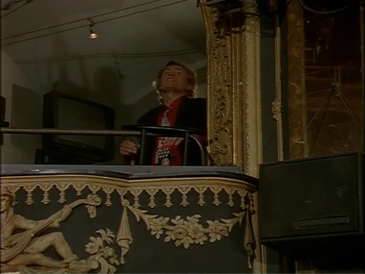 A Change of Place (1994) movie still: medium — An ornate theater balcony features gilded relief carvings of classical figures against black…