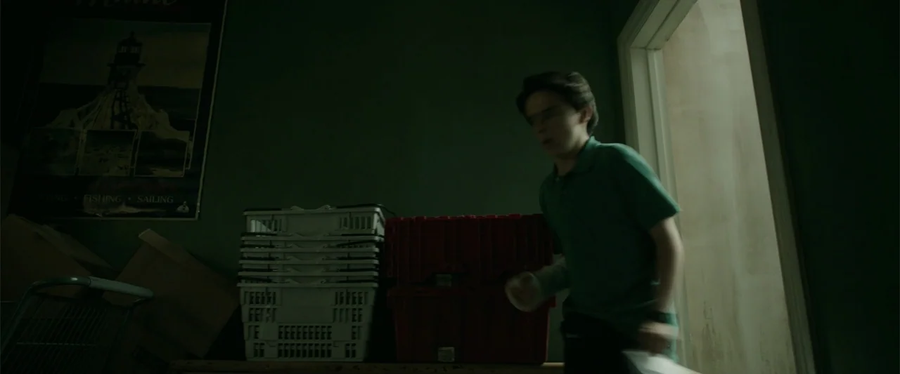 K.G.F: Chapter 2 (2022) movie still: medium — A dark storage room with green walls and stacks of plastic crates. A teenage boy walks quickly past…