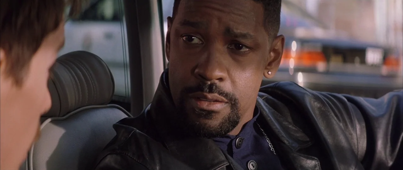 Training Day (2001) movie still: closeup — A dark sedan interior shows two men interacting while parked during the day. Denzel Washington looks…