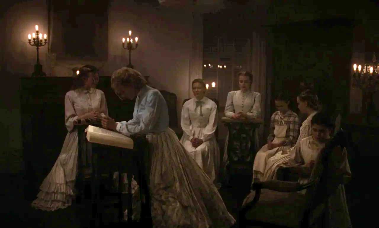 The Beguiled (2017) (2017) movie still: wide — A dark, dimly lit parlor room contains several women sitting in chairs. One woman stands by a small…