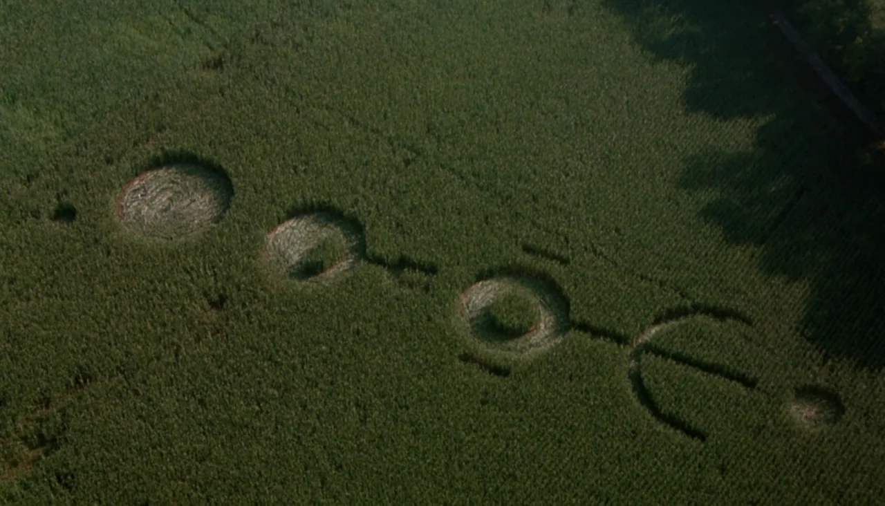 Signs (2002) movie still: establishing — An aerial view captures a vast field of dense, green growing corn crops. Geometric patterns consisting of…