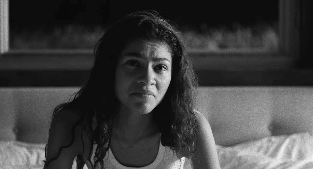 Malcolm & Marie (2021) movie still: closeup — A dark, blurred interior space provides a minimal backdrop behind a person. The subject rests on a…