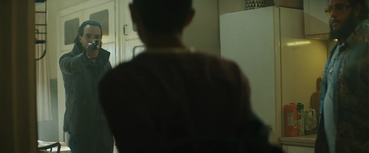 Black Adam (2022) movie still: medium — A residential kitchen features white cabinets, a refrigerator, and various groceries on the counter. A man…