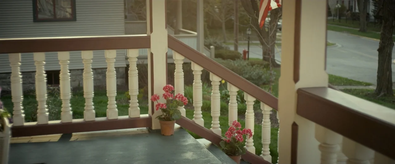 God Bless the Broken Road (2018) movie still: medium — A residential porch features painted white wooden railings and two terracotta pots with pink…
