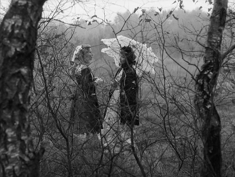 Effi Briest (1974) movie still: fullbody — Two women stand amidst a bare forest during late autumn or early spring. They are dressed in formal…