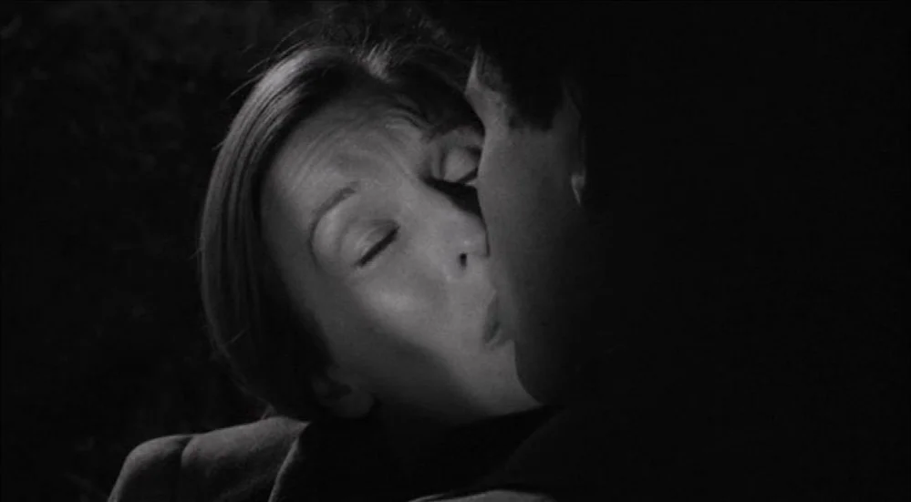The Last Picture Show (1971) movie still: closeup — A dark room is lit only by a soft light on the woman's face. The woman kisses a man whose face…