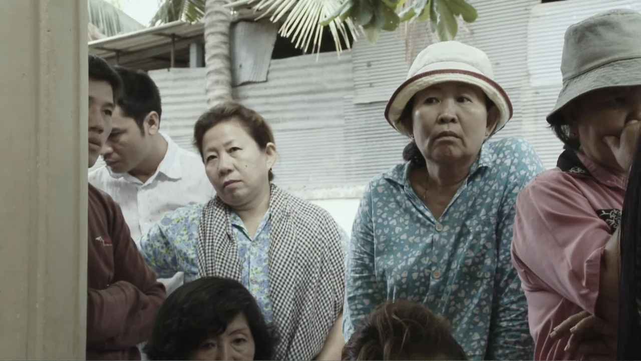 A Cambodian Spring (2018) movie still: medium — An outdoor gathering shows several individuals standing together in a crowded semi-enclosed space. A…