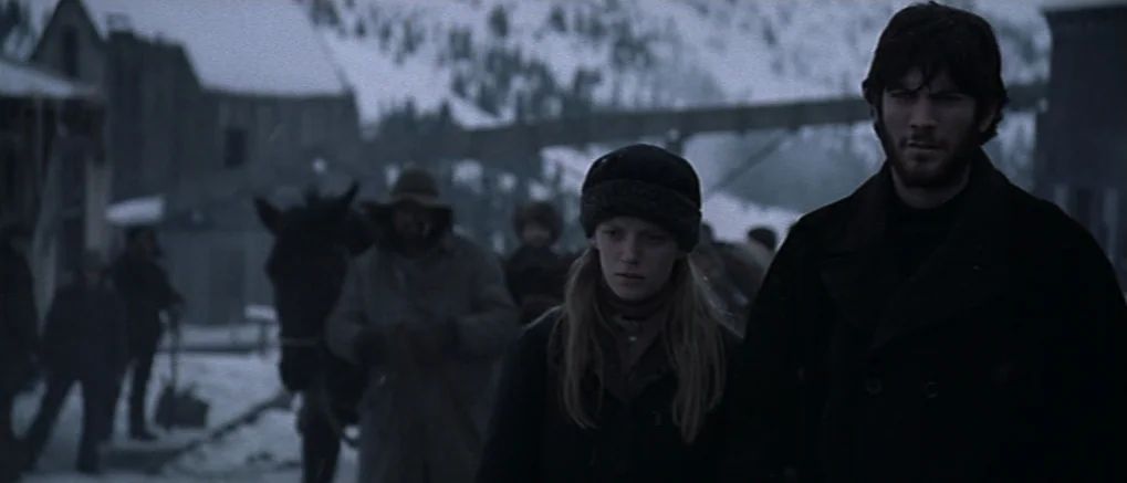 The Claim (2000) movie still: medium — A snowy, desolate western town street features wooden buildings and a horse. A young man and woman walk…
