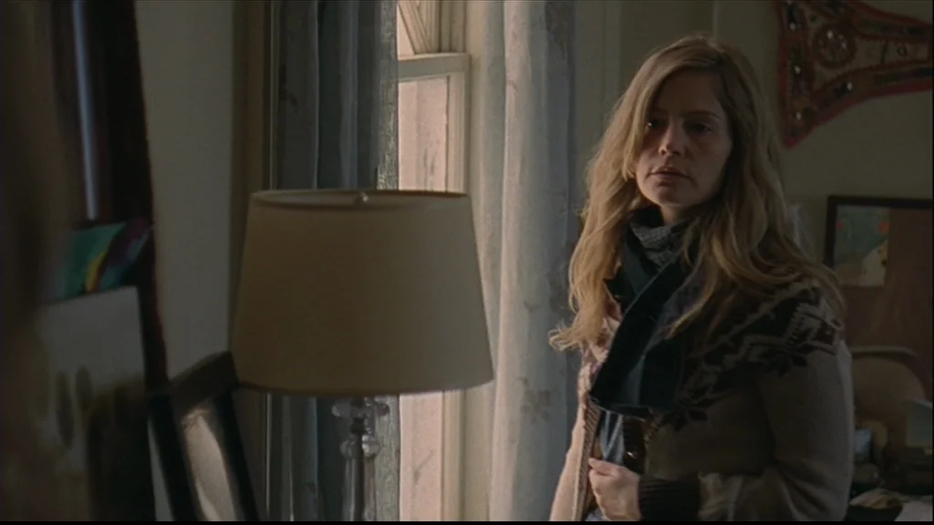 Margot At The Wedding (2007) movie still: medium — A woman stands in a domestic space next to a window with thin curtains. She wears a patterned…
