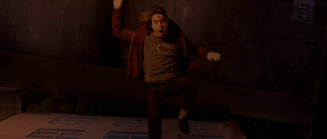Suitable Flesh (2023) movie still: medium — A man freefalls through the air past a dark concrete wall at night. He gestures wildly with his arms…