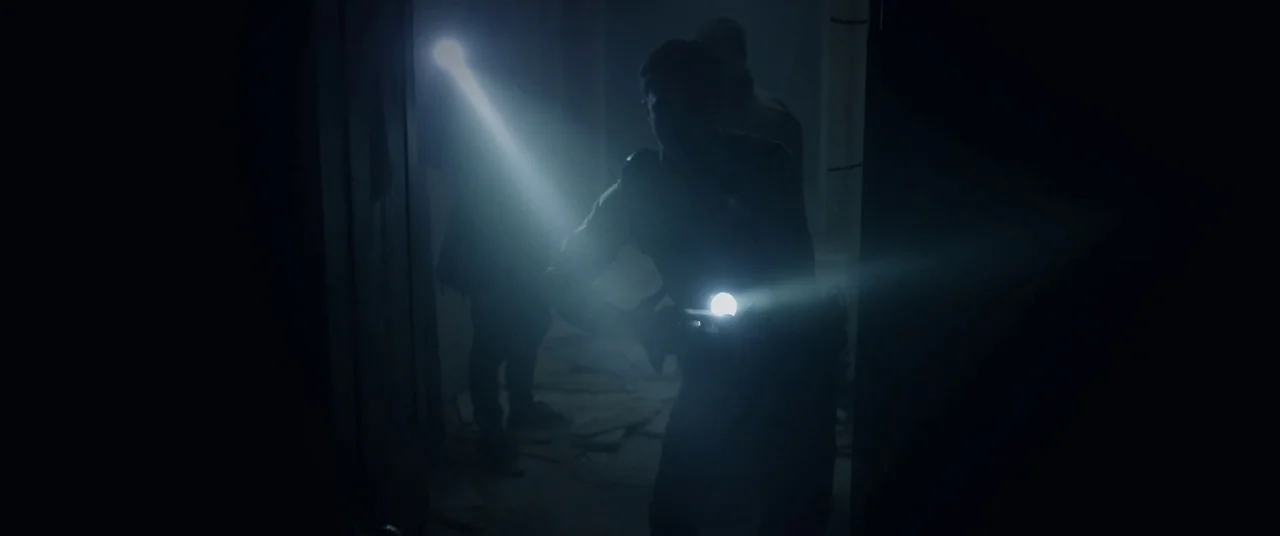 The Void (2016) movie still: medium — A darkened interior space appears covered in scattered debris and thick haze. A figure in the foreground aims…