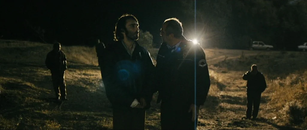 Once Upon a Time in Anatolia (2011) movie still: fullbody — A dirt path at night illuminated by the blinding light of a stationary vehicle. Two men…