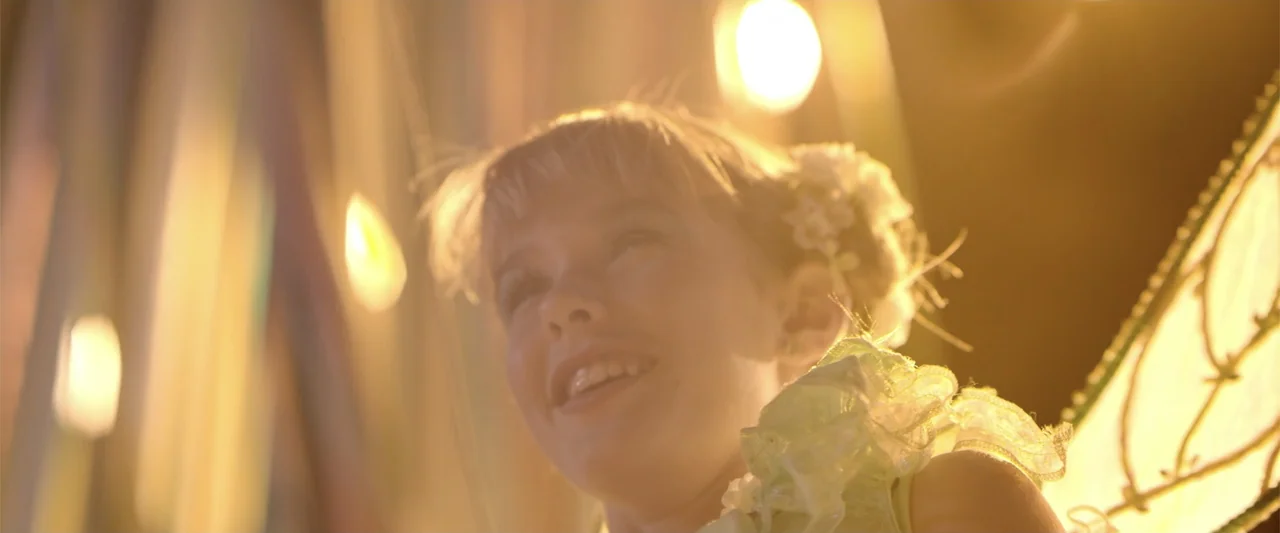 Dirty Little Secret (1998) movie still: closeup — A young girl with fairy wings is illuminated by warm, blurred festive lights. She looks upward…