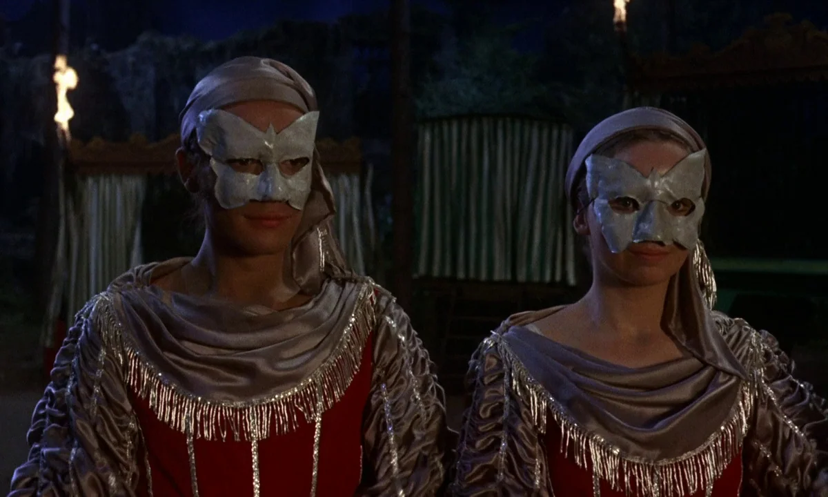 Vampire Circus (1972) movie still: medium — An outdoor night setting featuring a dark background with blurred structures behind the subjects. Two…
