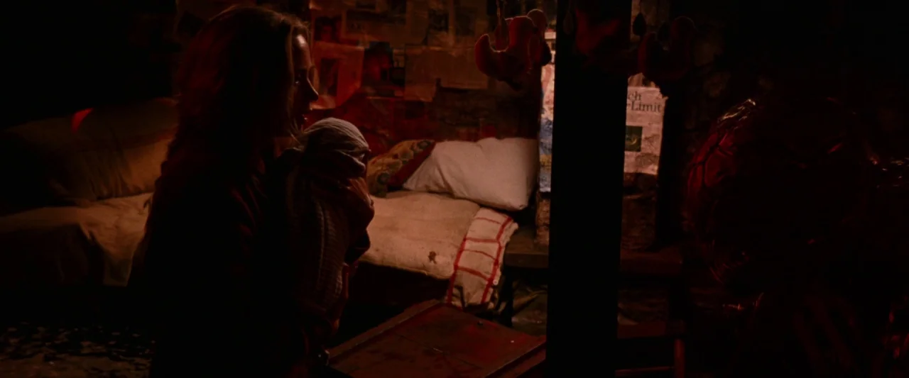 A Quiet Place (2018) movie still: medium — A dimly lit room filled with clutter, newspapers, and makeshift beds. A woman holds her baby while a…