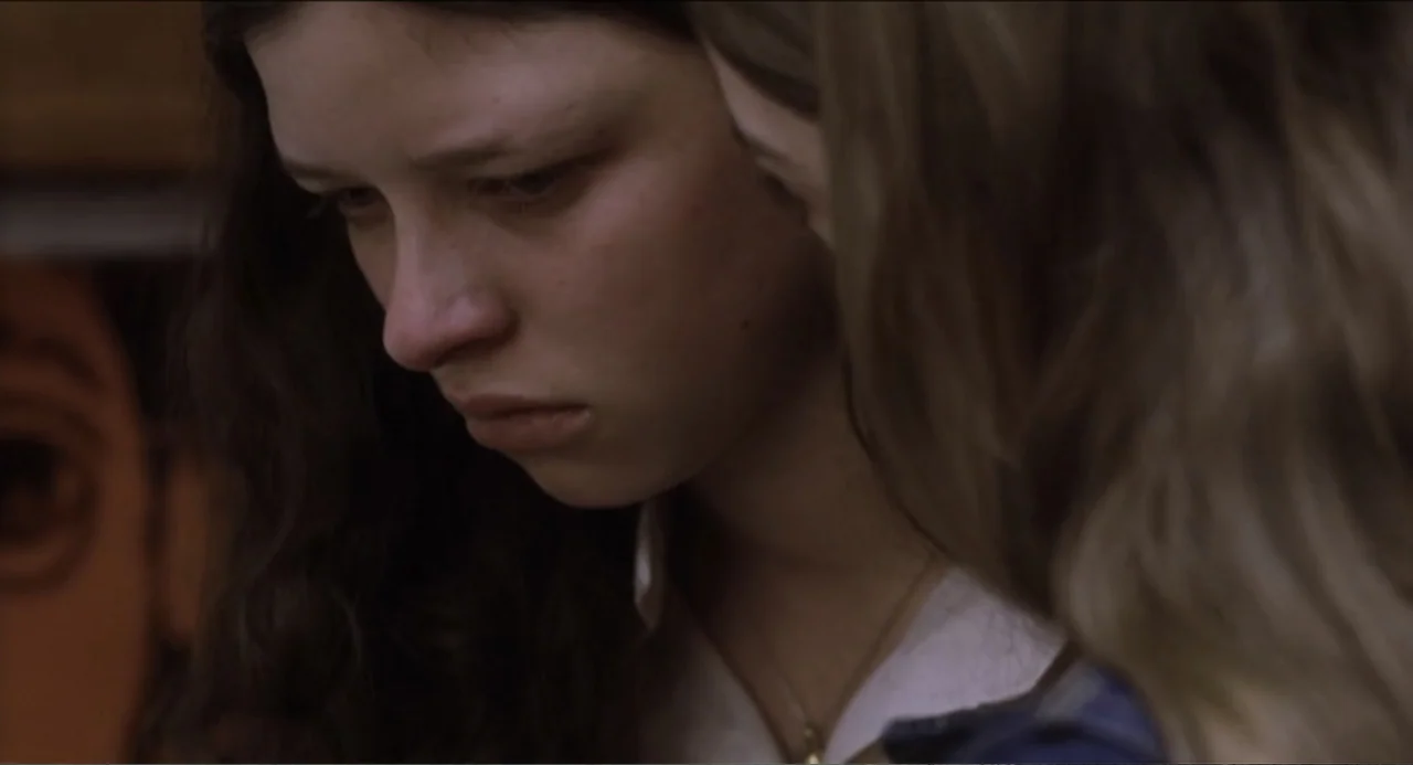 The Holy Girl (2004) movie still: closeup — Two young women stand close together in a dim, neutrally colored indoor environment. One woman with…