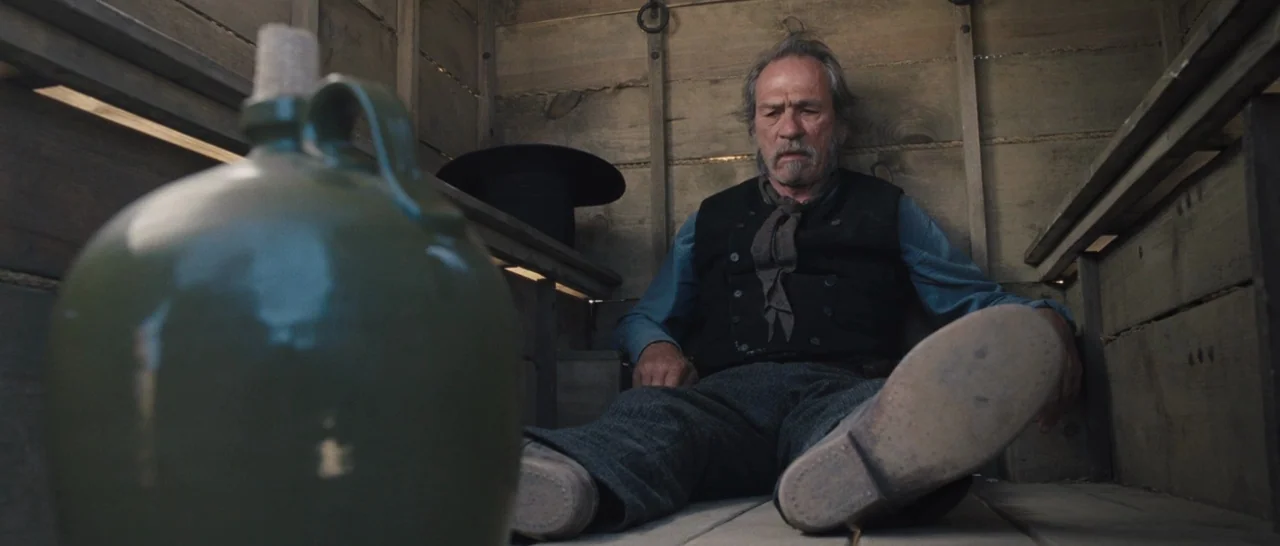 The Homesman (2014) movie still: medium — The interior of a wooden wagon with slat walls and floor planks. An elderly man with a mustache sits on…