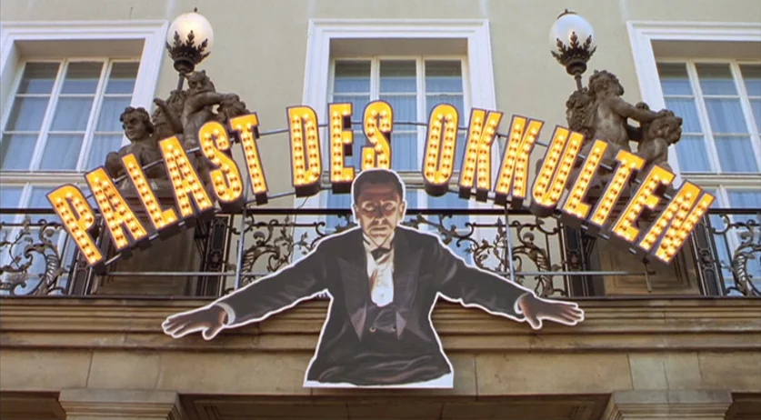 Invincible (2001) movie still: wide — A stone building facade features a wrought iron balcony and three tall arched windows. A large illuminated…