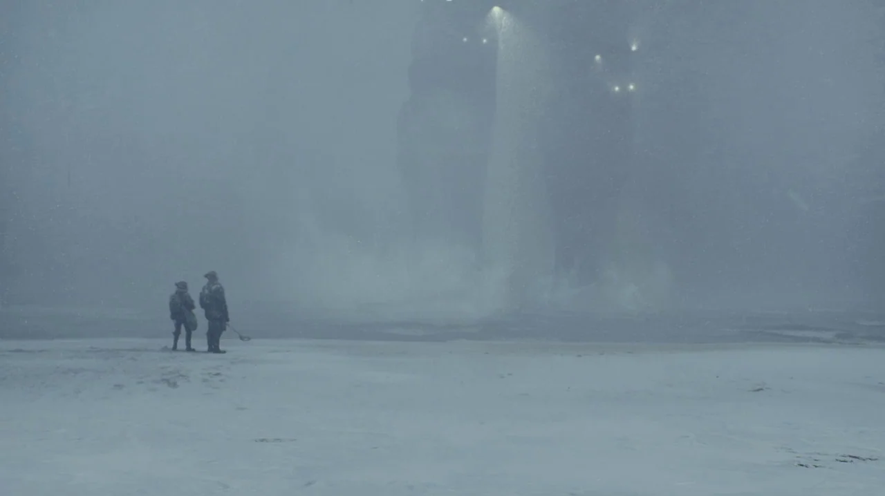 Pacific Rim (2013) movie still: wide — A vast, desolate, snow-covered landscape under a heavy, overcast, stormy sky. Two small human figures stand…