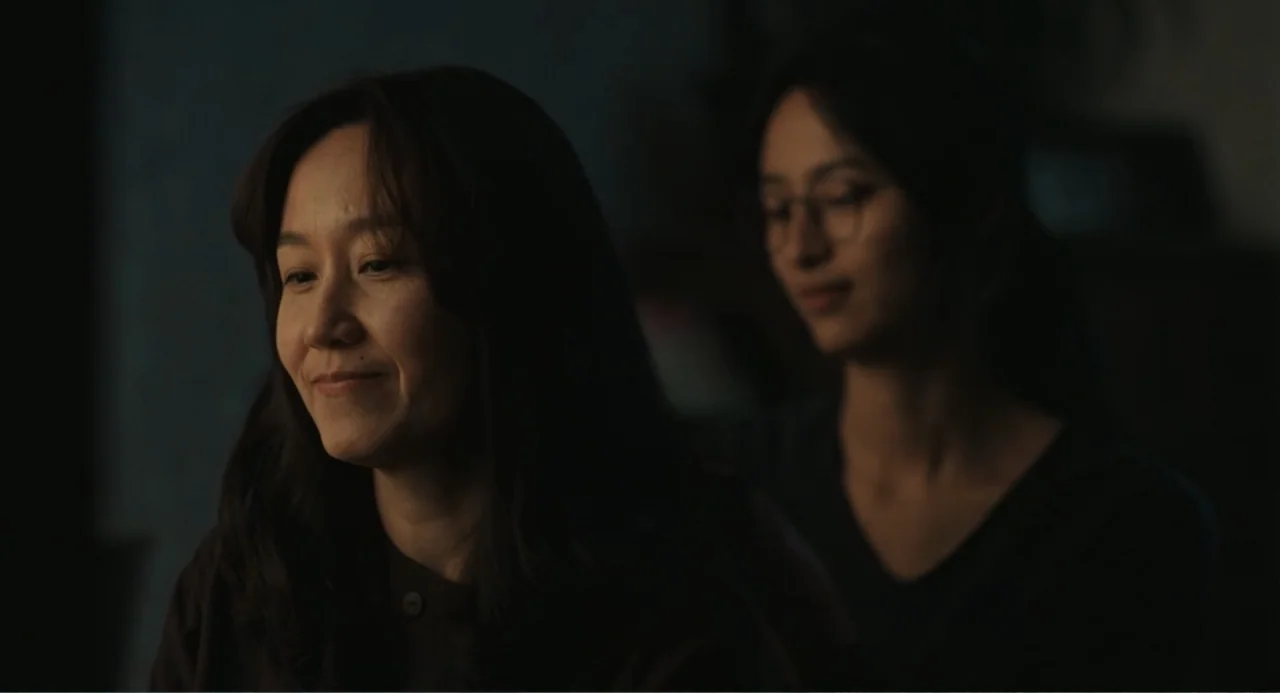 Winter in Sokcho (2025) movie still: medium — A dark indoor space with blurred furniture in the background. Two women are positioned with one seated…
