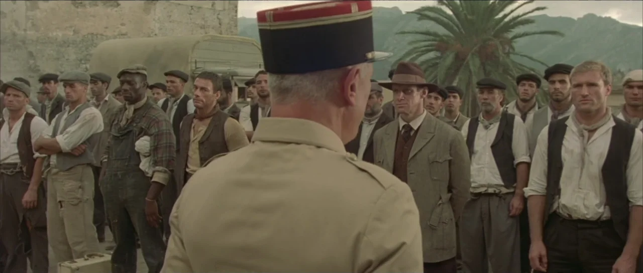 Legionario (2025) movie still: medium — A group of diverse laborers in 1920s workwear stands on a stone dock near a truck. An officer in uniform…