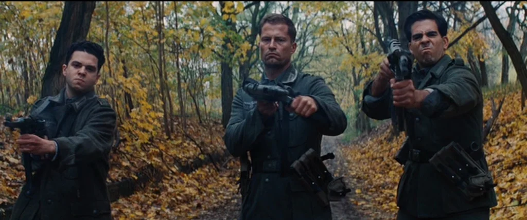 Inglourious Basterds (2009) movie still: fullbody — A narrow dirt path winds through a dense thicket of yellowing autumn trees. Three uniformed men…