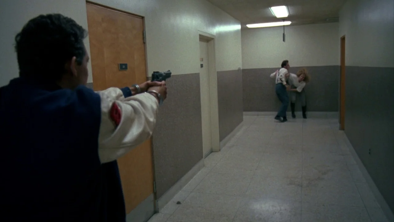 Jason Goes To Hell (1993) movie still: medium — A long beige corridor with fluorescent ceiling lights and multiple brown wooden doors. A man points…