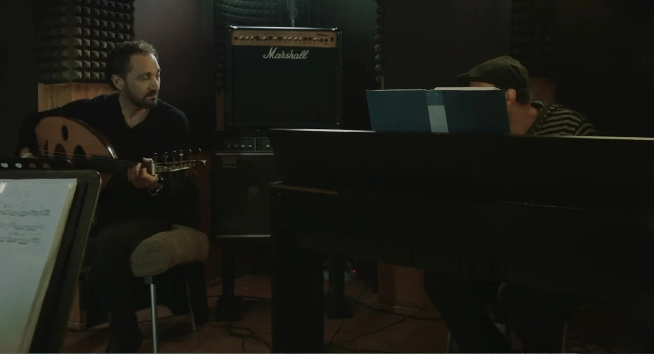 Cairo Jazzman (2017) movie still: medium — A dimly lit room with acoustic foam wall panels contains two musicians with instruments. One man plays an…