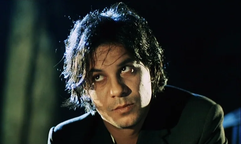 The Rose King (1986) movie still: closeup — A man stands in a dark, outdoor setting with minimal ambient light visible behind him. The man looks…