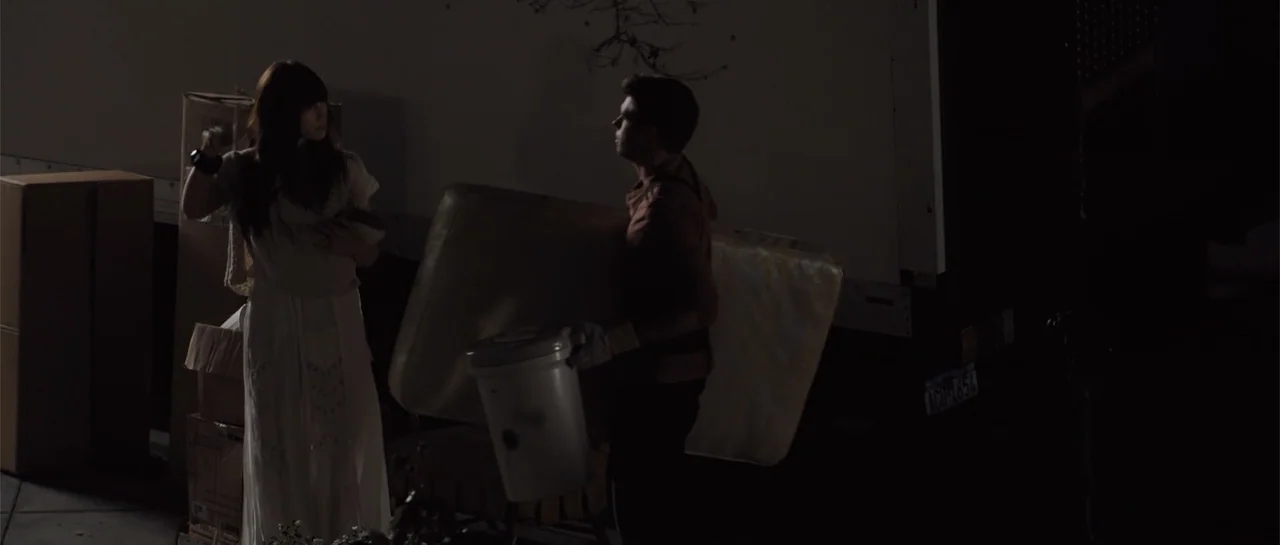 The Truth About Emanuel (2013) movie still: medium — A dark loading dock at night features cardboard boxes and a large truck trailer. A man carries…
