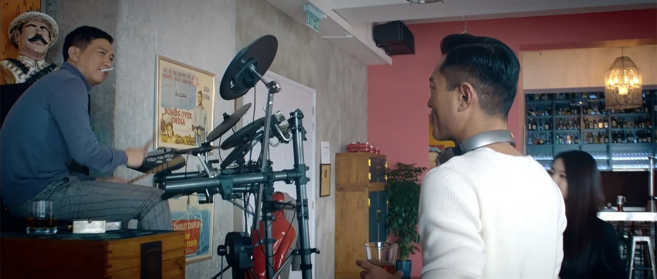 Line Walker (2016) movie still: medium — A room with pink walls and a concrete pillar features electronic drum equipment. One man plays drums while…