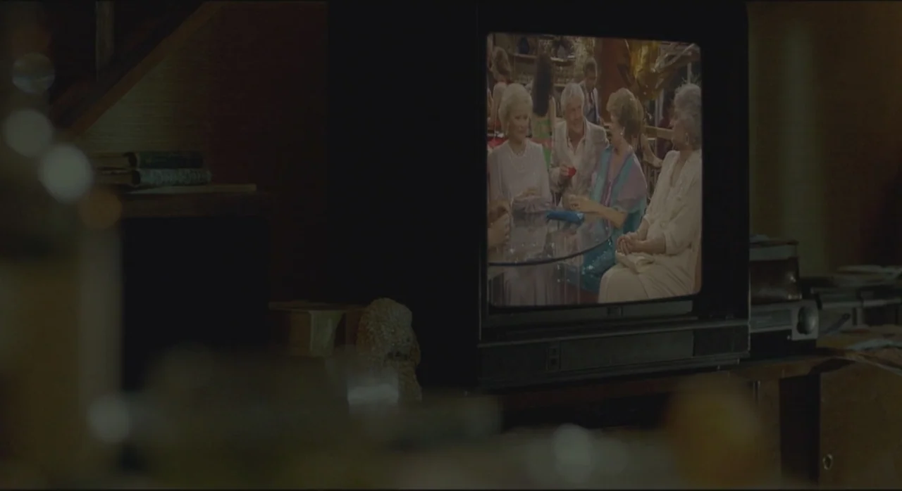 St. Vincent (2014) movie still: medium — A dimly lit room focuses on a vintage television set displaying a colorful program. Four people are…