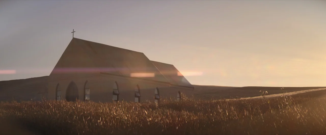 The New Boy (2023) movie still: establishing — A small isolated church with a cross on the roof stands in a field. The building is surrounded by…