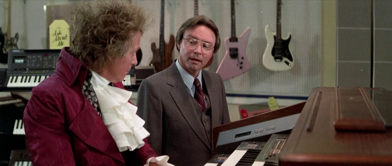 Bill and Ted’s Excellent Adventure (1989) movie still: medium — A retail music store with electric guitars mounted on a white pegboard wall behind.…