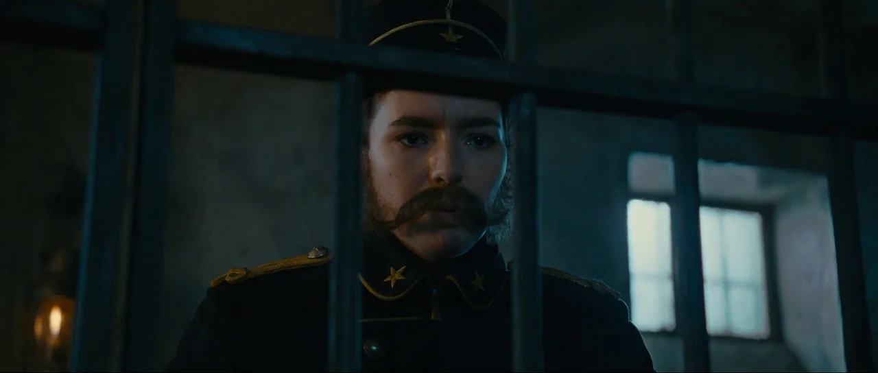 The Extraordinary Adventures of Adèle Blanc-Sec (2010) movie still: medium — A dimly lit room viewed through thick vertical iron bars. A man in…