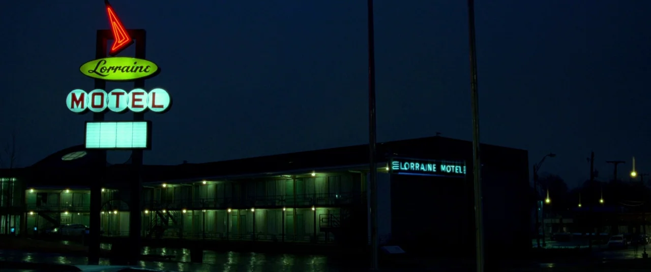 Mississippi Grind (2015) movie still: establishing — A dark night exterior features the iconic Lorraine Motel with its glowing neon signage. The…