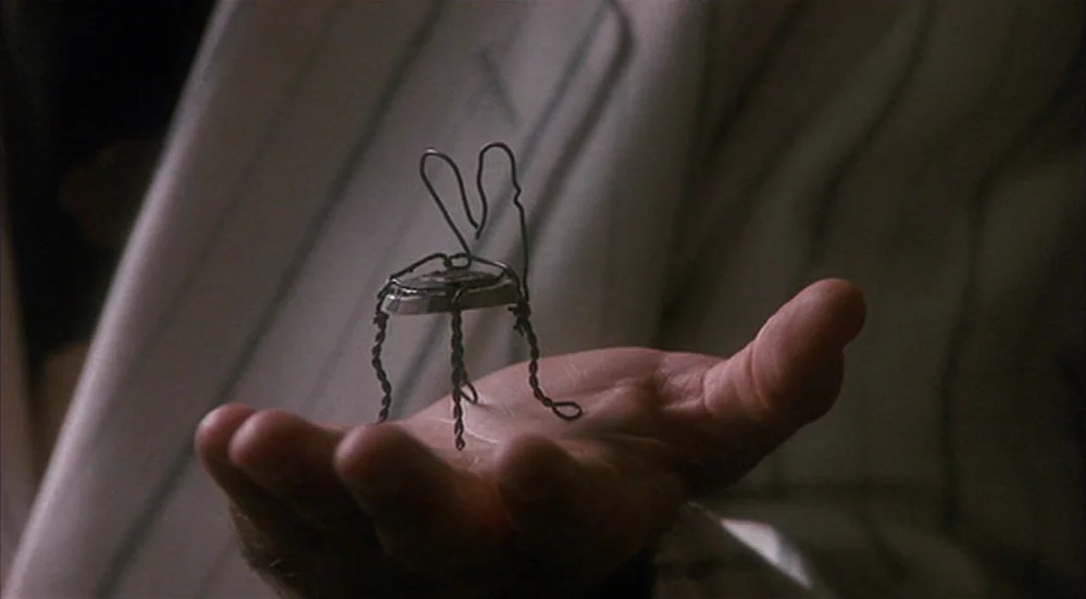 The Fisher King (1991) movie still: closeup — A close-up of a human palm holding a small sculpture made of twisted wire. The sculpture is shaped…