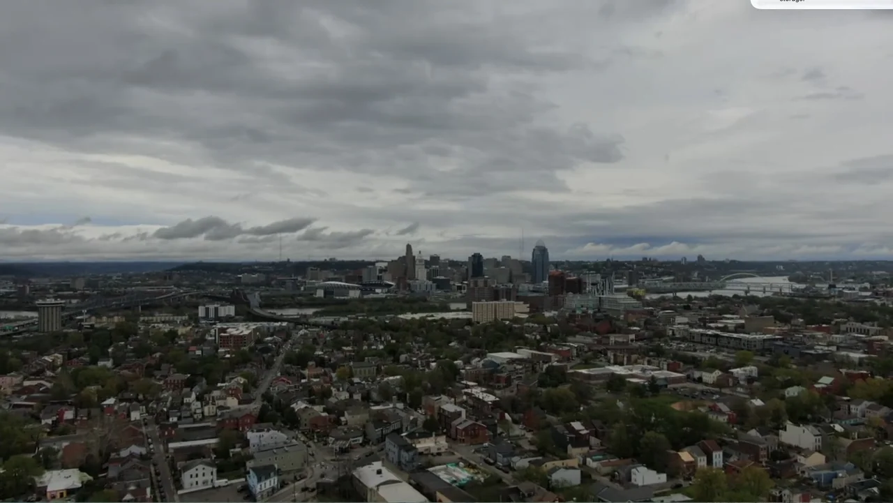 Murder at Carter County Mines (2023) movie still: establishing — An aerial view of a dense city skyline under a thick grey cloud cover. Residential…